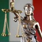 Estátua da justiça com a bandeira da Itália ao fundo.